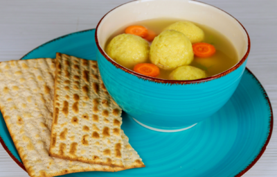 Blue bowl of matzo ball soup with carrot slices, served on a matching plate with matzo crackers.