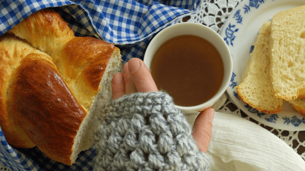 A person's hand reaching for a loaf of challah and a cup of honey