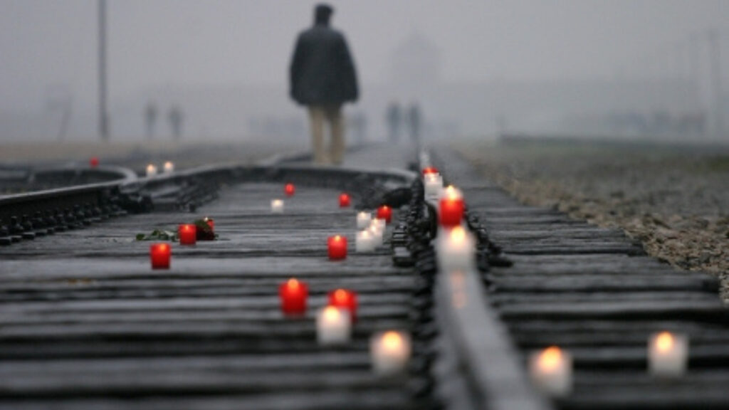Lit red and white candles on railroad tracks with person silhouetted in foggy background