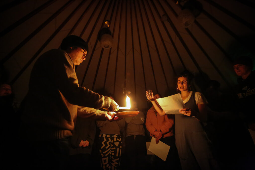 People in a dimly lit room gathered around a central candle flame, engaging in a group activity.