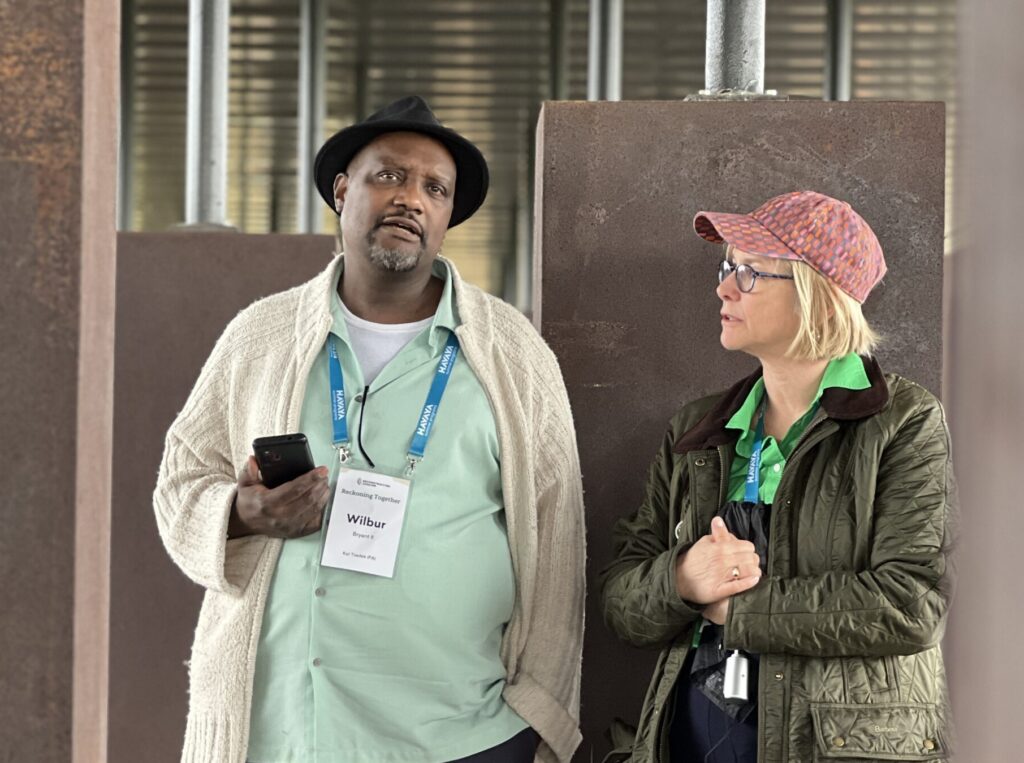 Two people standing and talking; one holds a phone and wears a name badge.