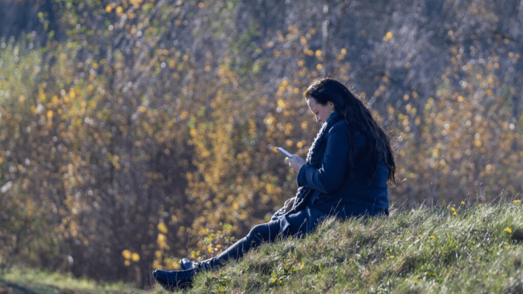 Woman sitting outside on a hill while on her phone