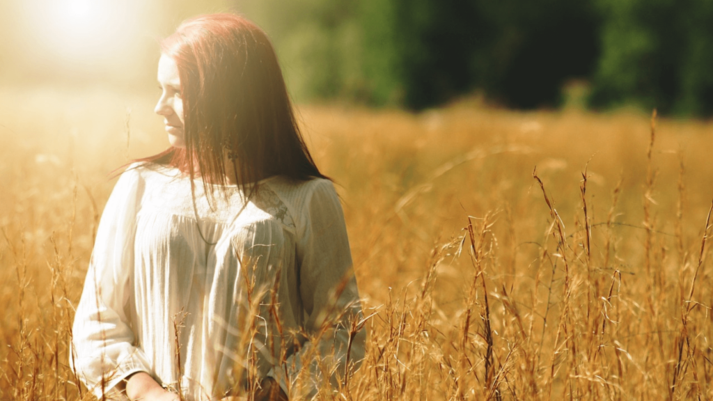 Woman walking through a field of wheat with the sun glare on her face