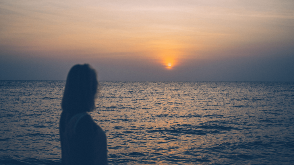 Silhouette of a woman watching the sun set over the ocean