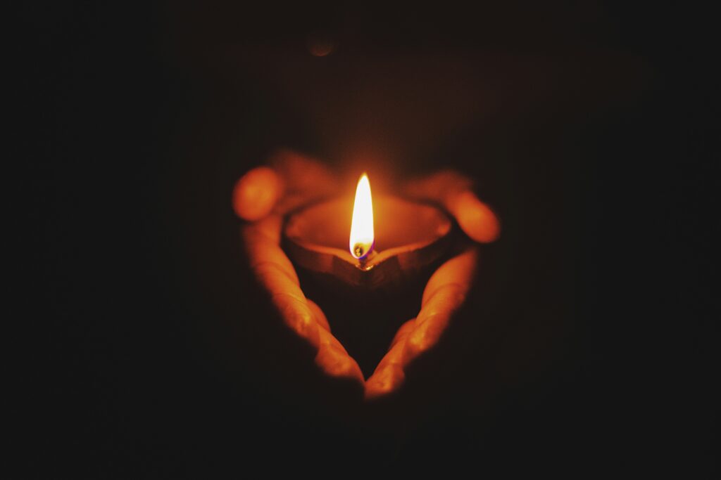 Hands holding a lit candle in the dark, forming a heart shape with their silhouette.