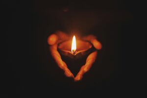 Hands holding a lit candle in the dark, forming a heart shape with their silhouette.