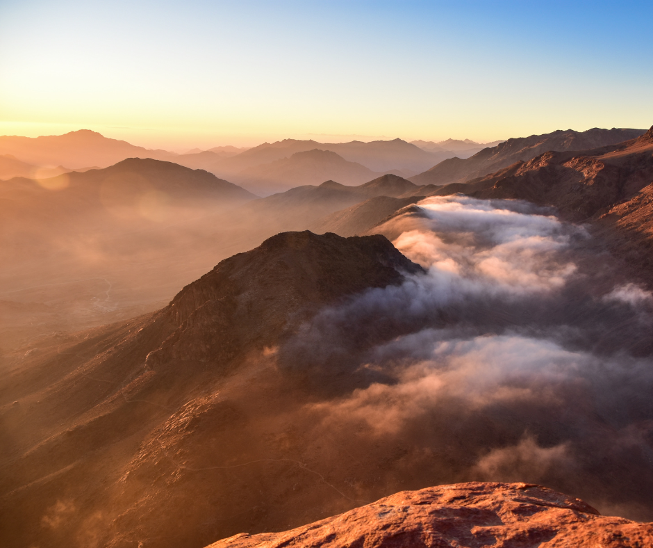 Sunrise over mountain range with rolling clouds and a vibrant sky casting warm light on the rugged peaks.