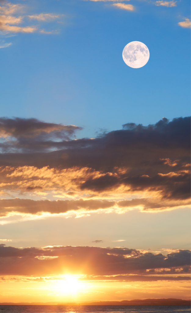 Sunset over the ocean with a full moon in the sky and scattered clouds.