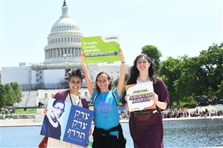 Three people hold advocacy signs in front of the U.S. Capitol building on a sunny day.