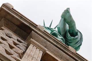 Low-angle view of the Statue of Libertys arm and torch against a cloudy sky, seen from the pedestal.