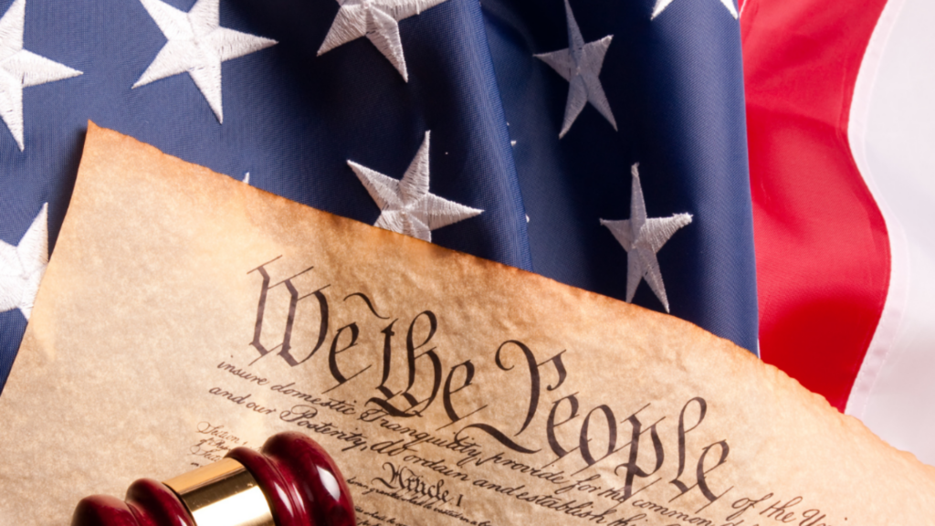 U.S. Constitution preamble with a gavel, in front of an American flag background.