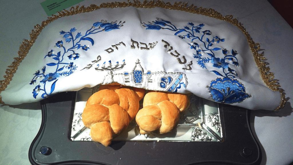 Two challah loaves covered by a blue and white embroidered cloth