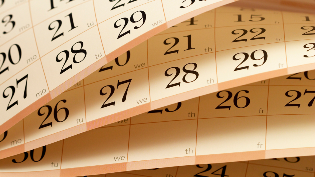 Close-up of overlapping calendar pages displaying dates in black on a beige background.