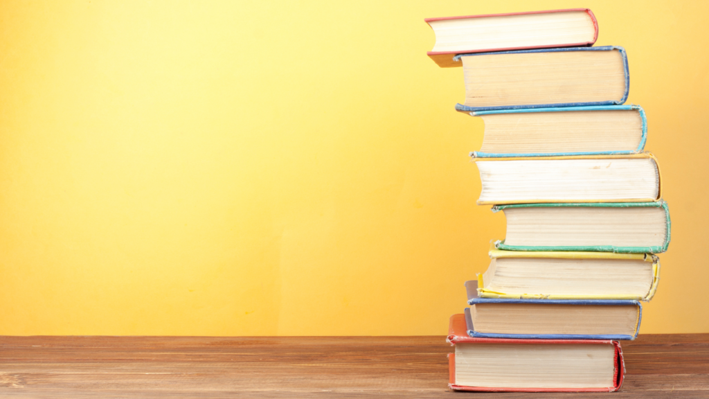 Stack of colorful books on a wooden surface against a bright yellow background.
