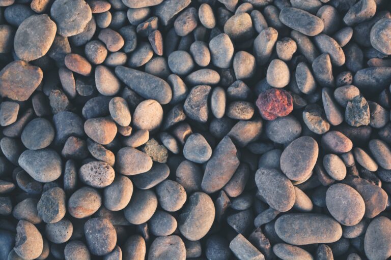 A collection of smooth, varying-sized gray stones with one distinct rusty red stone among them.