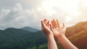 Hands raised towards the sky against a backdrop of mountains and clouds.