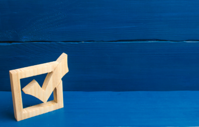 A wooden checkmark stands on a blue wooden surface with a matching blue background.