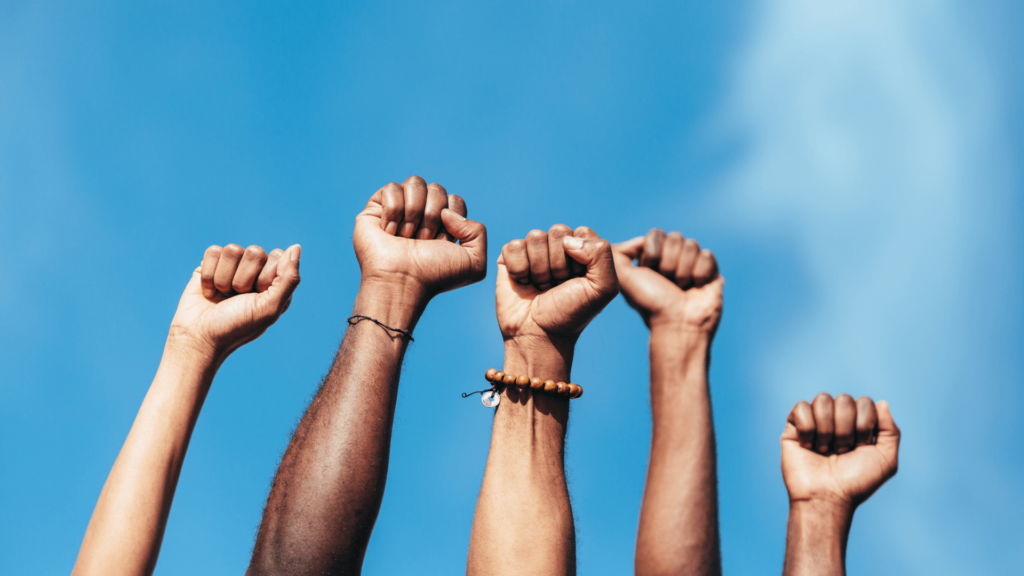 A multicultural group of people's fists raised against a blue sky