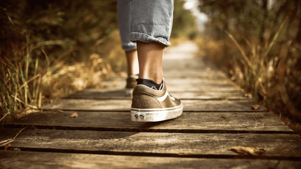 Close-up of a person's feet in sneakers walking on a wooden plank path