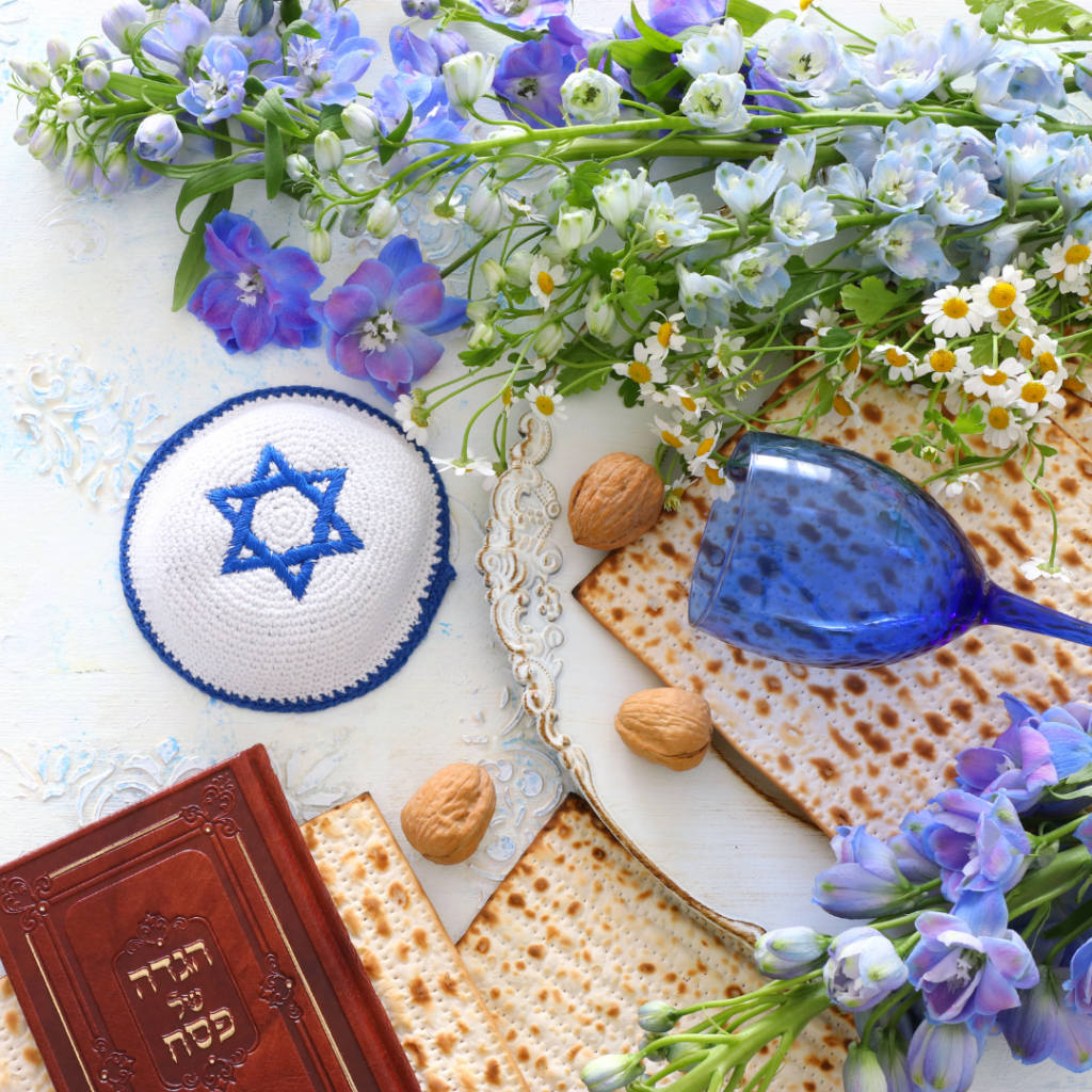 Passover items with matzah, kippah, blue goblet, and flowers arranged on a white background.