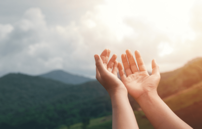 Open hands against a hilly background and a cloudy sky