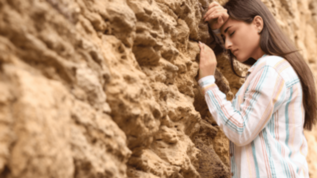 A sad woman leaning against a rocky wall