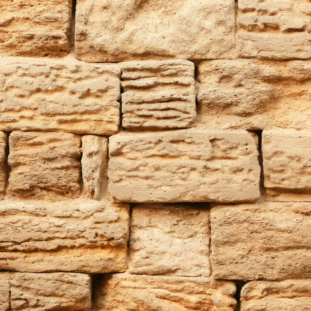 Close-up of a textured stone wall with irregularly shaped, weathered bricks in shades of beige and brown.