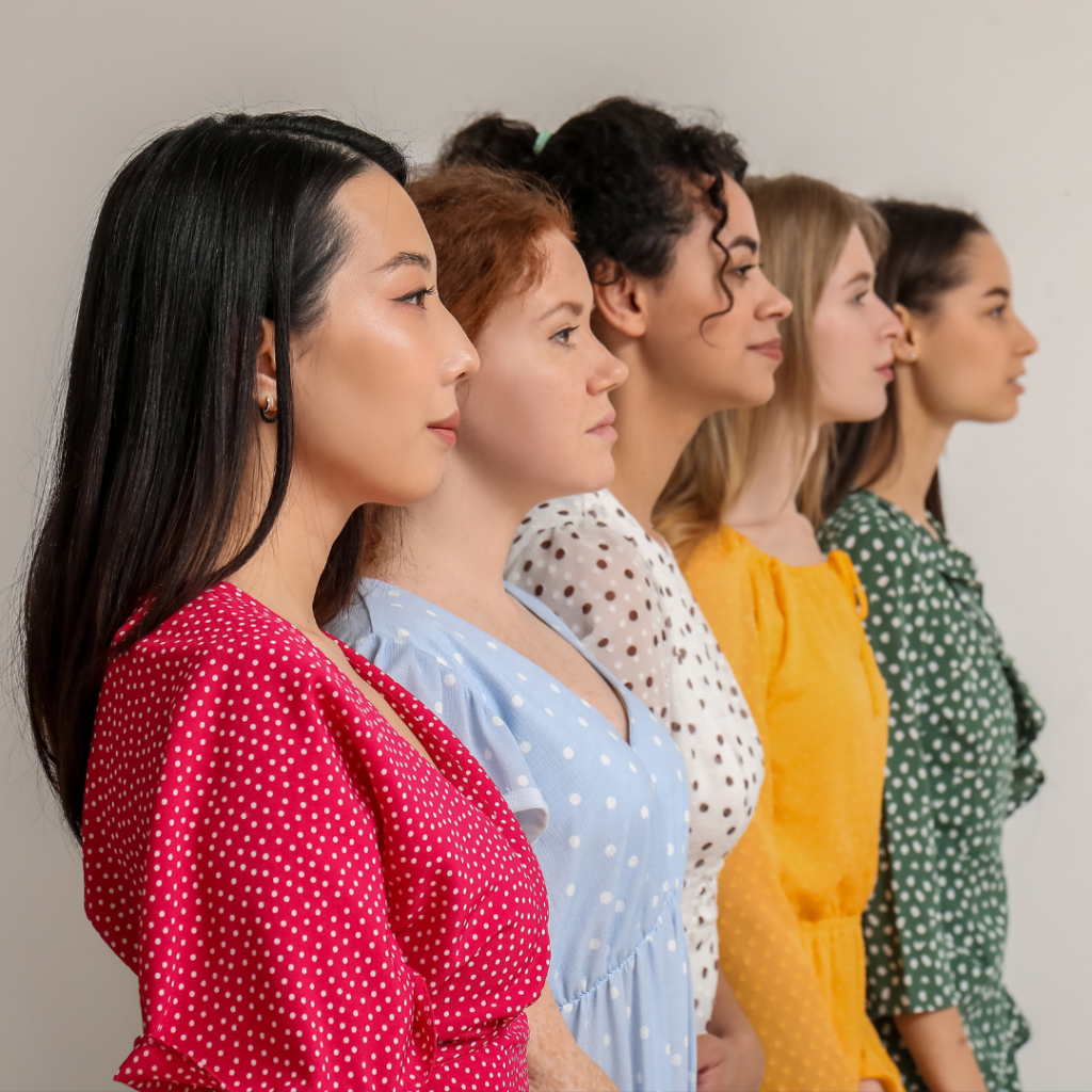 Five women in profile wearing colorful polka dot dresses stand in a line against a white background.