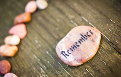 Smooth stone with Remember engraved on it, surrounded by smaller stones on a wooden surface.