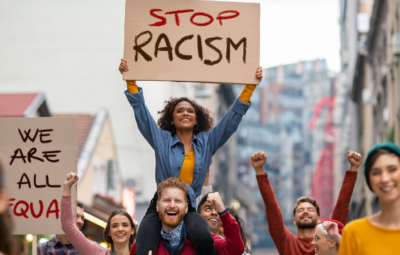 Diverse group of people marching, holding signs that read Stop Racism and We Are All Equal, expressing unity.