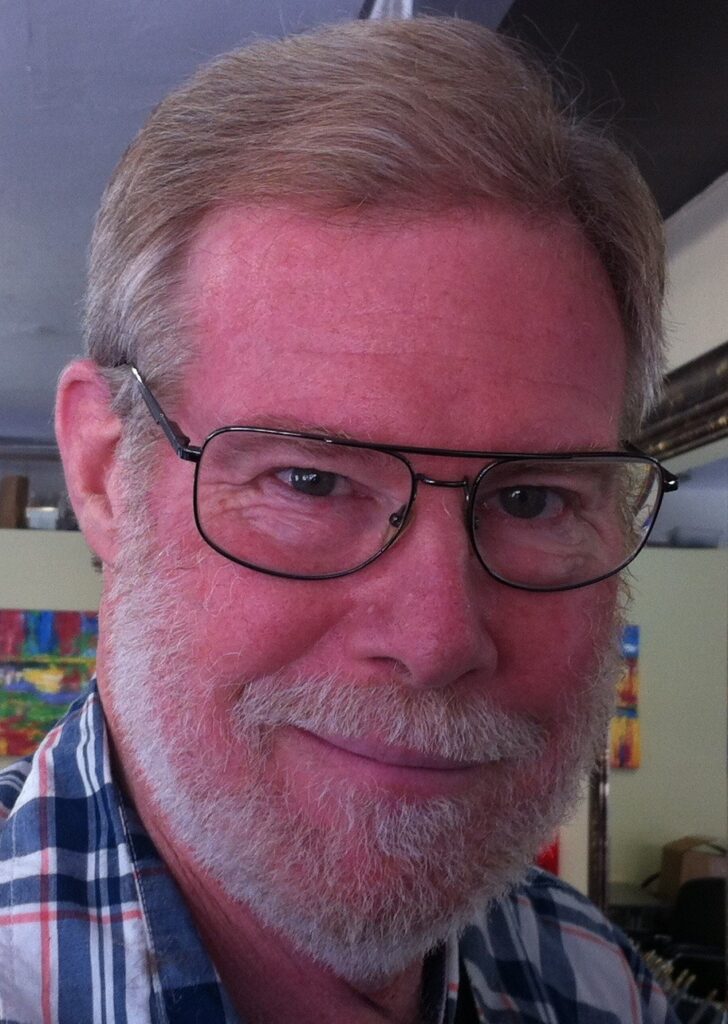 A man with glasses, a beard, and wearing a plaid shirt, smiling at the camera.