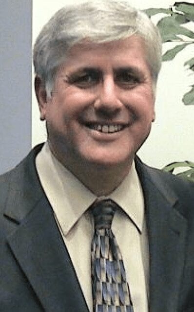 Smiling man in a suit and tie standing in front of a plant.