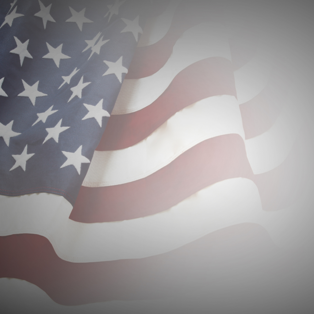 Faded American flag waving with stars and stripes visible on a blurred, gray background.