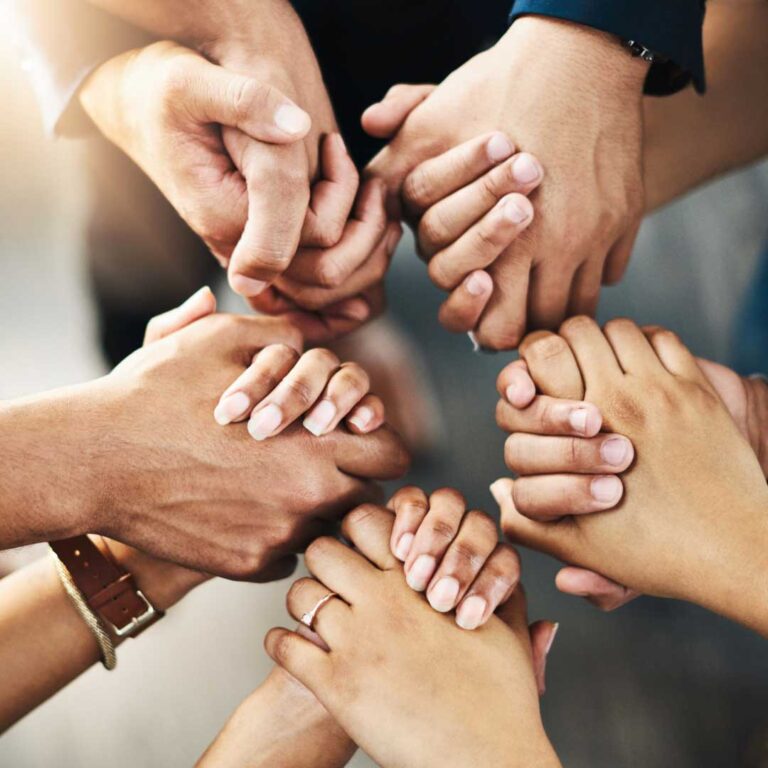 A circle of diverse hands clasped together, symbolizing unity and teamwork.