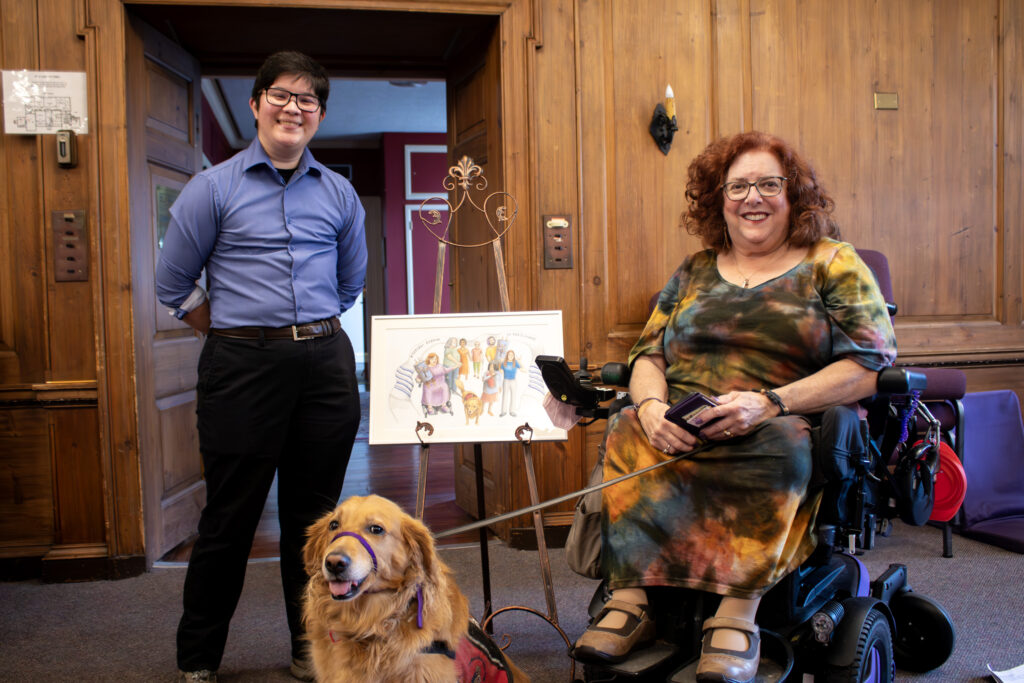 Rabbi Asher Sofman, Wendy Elliott-Vandivie and d her service dog with her artwork in the Reconstructionist Rabbinical College's community space.