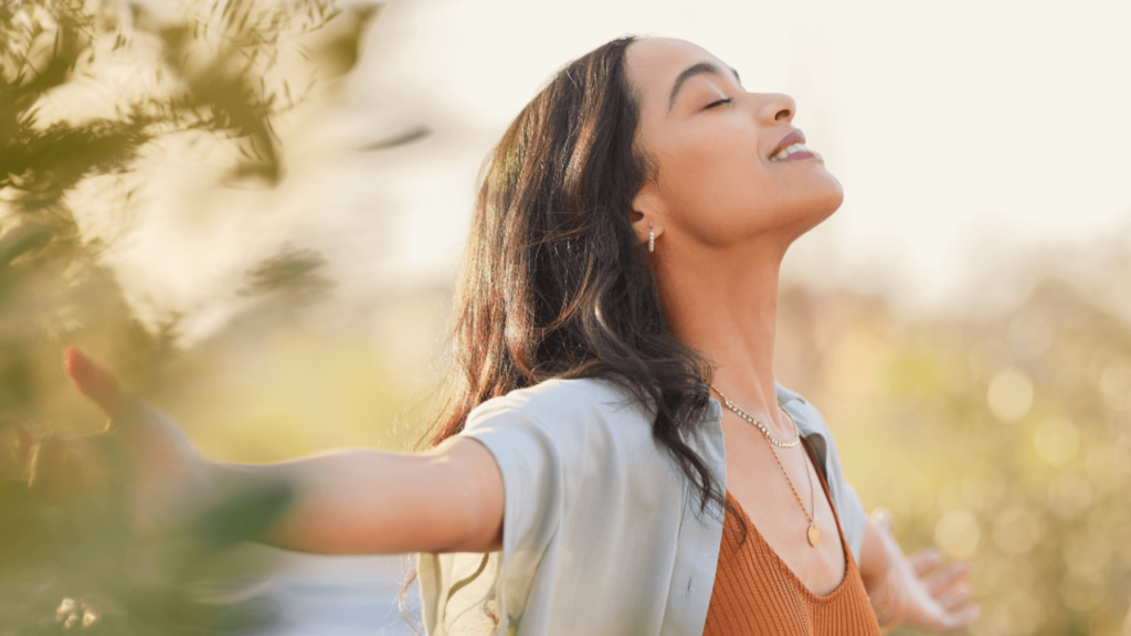 A woman with her eyes closed and her arms open outside