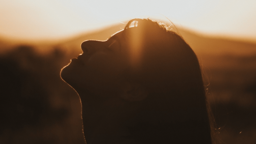 A woman's upturned face in profile silhouetted in sepia against an outdoor background