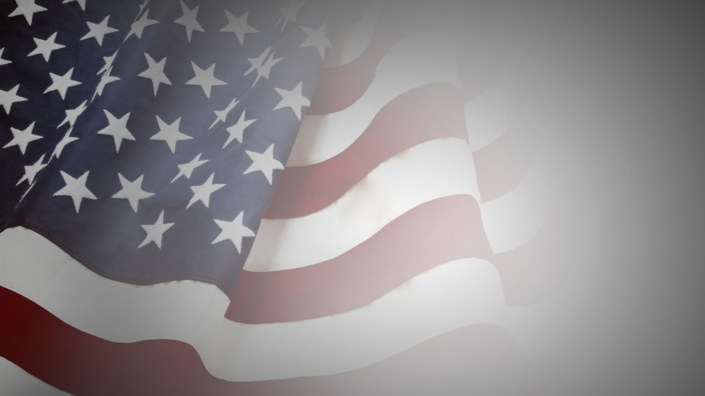 Close-up of a waving American flag with visible stars and stripes, blending into a gray gradient background.