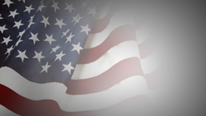 Close-up of a waving American flag with visible stars and stripes, blending into a gray gradient background.