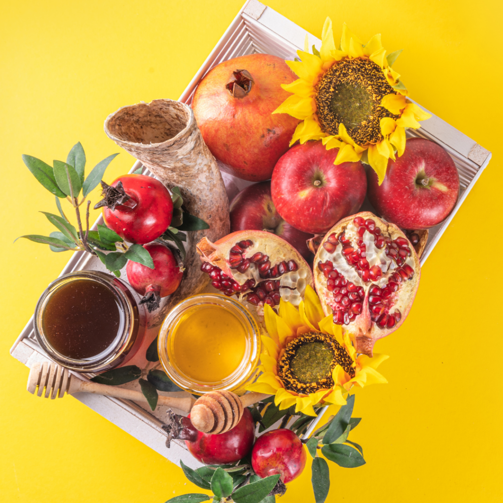 Tray with honey, apples, pomegranates, sunflowers, and leafy greens on a bright yellow background.