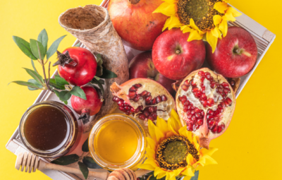Tray with honey, apples, pomegranates, sunflowers, and leafy greens on a bright yellow background.