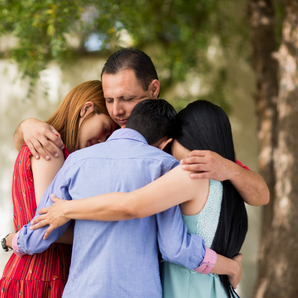 Four people embracing in a group hug under a tree.
