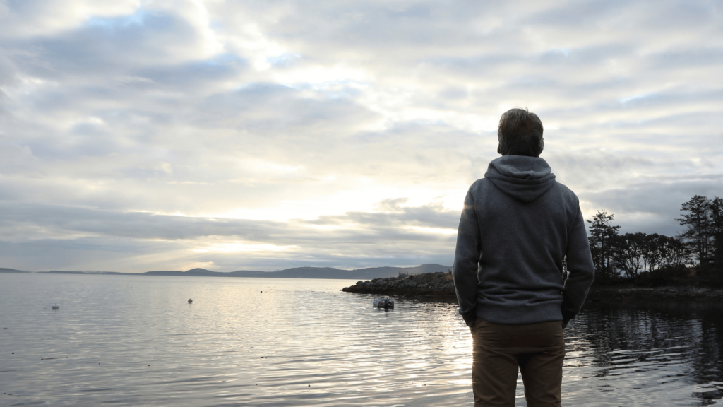A person looking out at a lake under a cloudy sky