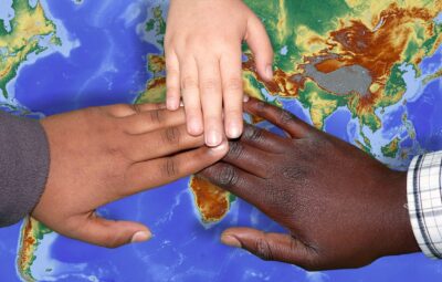 Three hands of different skin tones touching over a world map background.