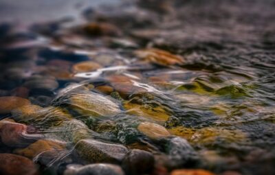 Close-up of clear water flowing over colorful, smooth pebbles in a shallow stream.