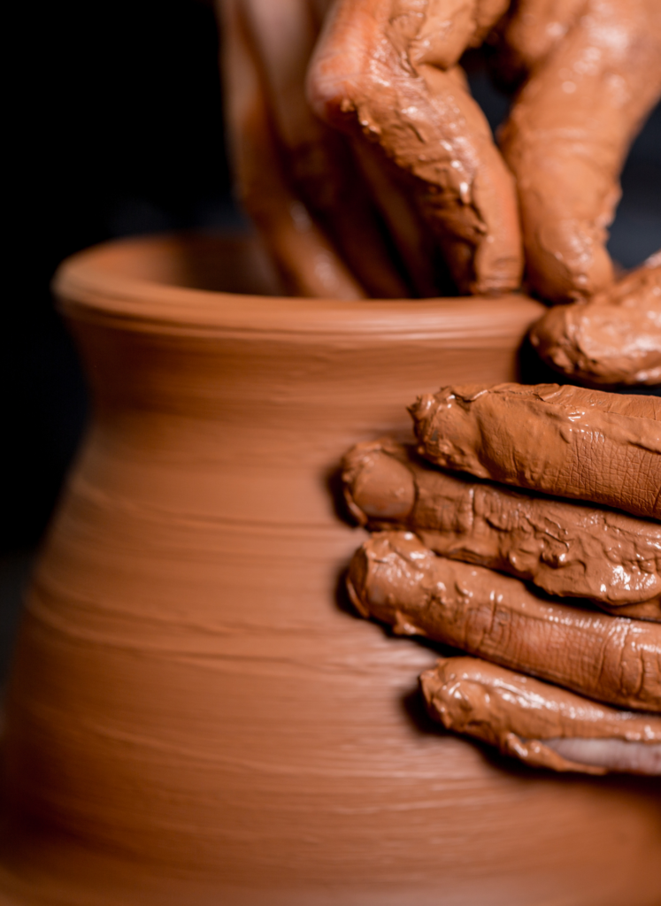 Hands shaping clay on a pottery wheel, crafting a pot.