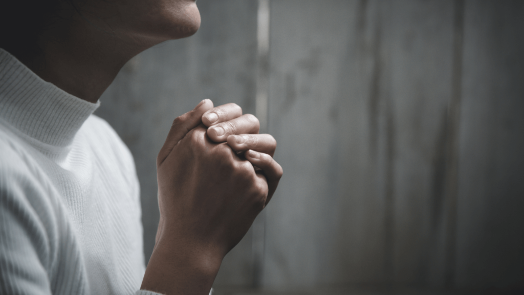 Close-up of a person in a white shirt with their hands clasped in prayer