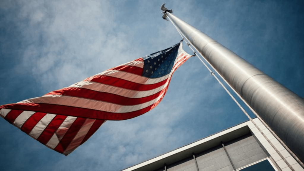 View looking up at an American flag waving on a flagpole outside of a building