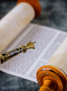 A Torah scroll partially unrolled, with a yad (pointer) highlighting text on the page.