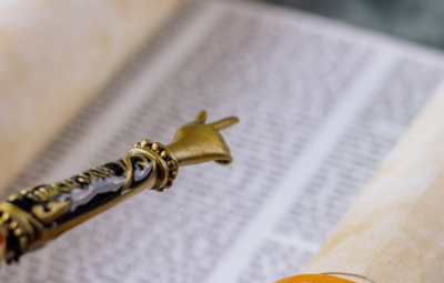 A Torah scroll partially unrolled, with a yad (pointer) highlighting text on the page.